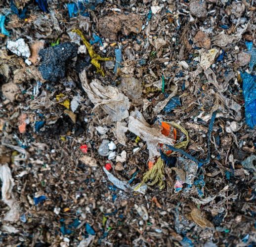 Close-up of mixed waste material with dirt, shredded debris, and small pieces of plastic.